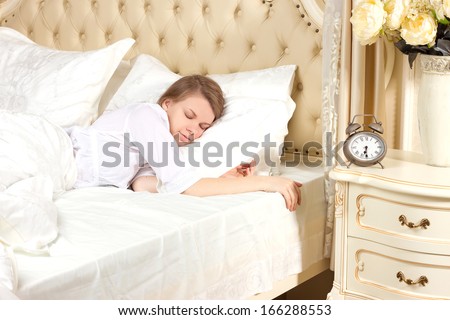 Beautiful sleeping woman resting in bed with alarm clock ready to wake her in the morning.