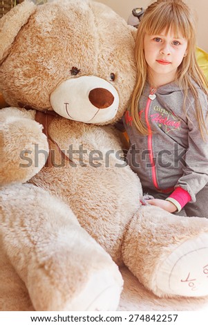 little girl hugging big teddy bear while sitting on chair