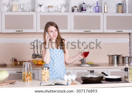 girl in the kitchen wearing an apron over his naked body with a glass of red wine on the phone. Horizontal framing