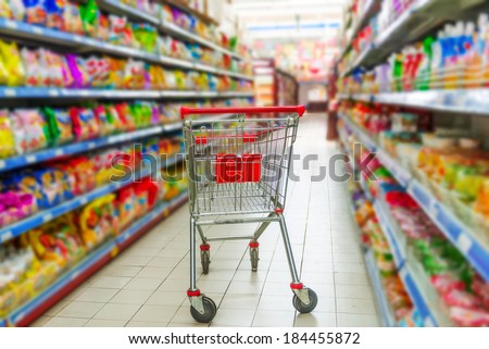 Supermarket interior, empty red shopping cart.