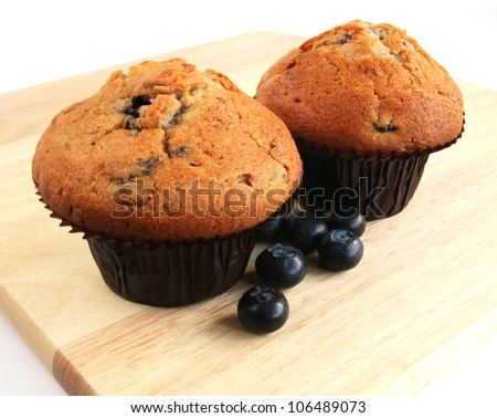 Blueberry muffins with fresh fruit on wooden board Closeup of two blueberry muffins with fresh blueberries on a wooden board