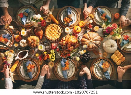 Group of friends or family members giving thanks to God at festive turkey dinner table together. Thanksgiving celebration traditional dinner concept