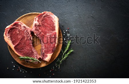 Heart shape raw dry aged beef rib steaks (cote de boeuf) with rosemary, pepper and salt on dark background