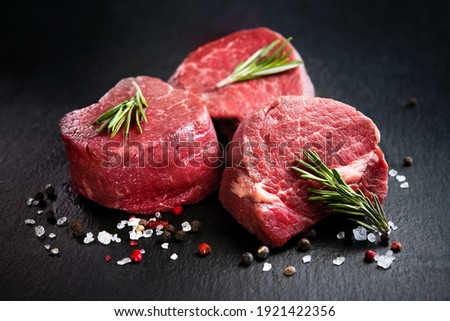 Raw beef filet mignon steaks with rosemary, pepper and salt on dark rustic board, black angus meat