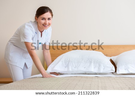Hotel room service. Young maid changing bedclothes in a room