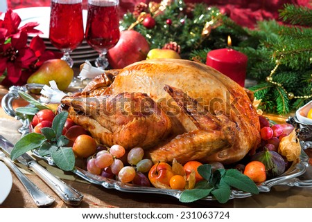 Roasted turkey on holiday table, candles and Christmas tree with ornaments