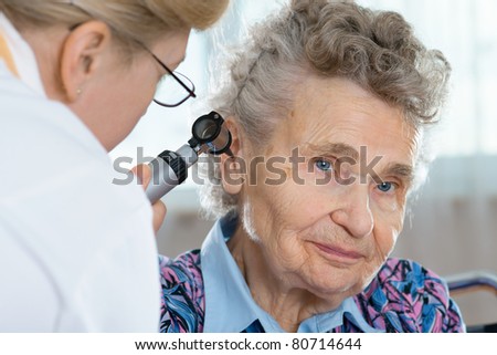Doctor performing ear exam with otoscope on a  senior patient