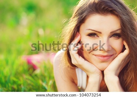 Close portrait of beautiful young woman on green grass in the summer outdoors