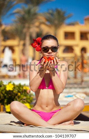 Beautiful young woman with strawberry in her hands in sun glasses sitting near swimming pool on sun lounger