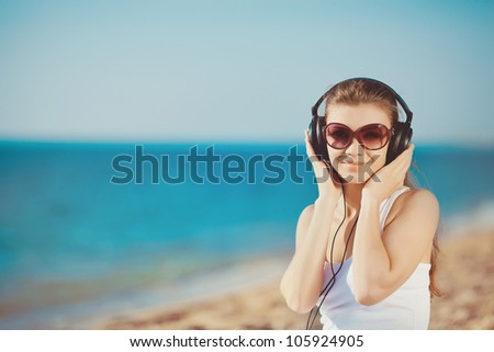 Beautiful woman listening to music near the water in headphones on the seashore