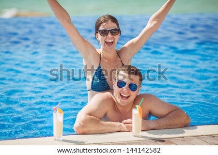 Beautiful couple drinking cocktails, hugging and kissing in the swimming pool on tropical resort