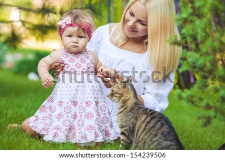 Young mother with child and a cat having fun on green lawn on summer day