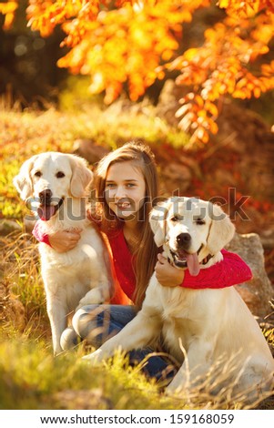 A beautiful woman and her dogs (Labrador retriever) posing in autumn park. Red and orange leaves around.