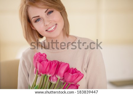 Beautiful young blond woman with tulip bouquet. Spring portrait. Bright pink flowers in girl\'s hands. At home. Interior portrait/