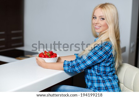 Smiling young woman sitting with laptop in modern kitchen with bowl strawberry