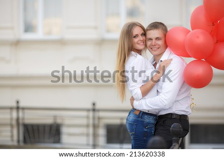 summer holidays, celebration and dating concept - couple with colorful balloons in the city. Young couple kissing among white columns and holding bunch of balloons