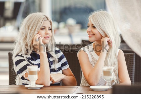 Two young women having coffee break together use smart phone. Happy women using cell phone at sidewalk cafe