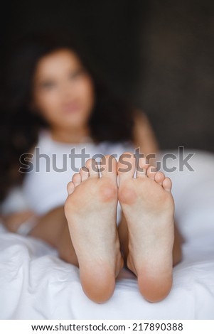 Beautiful feet of a young woman lying in bed close up. Woman Holding her Tired Feet in Hand Sitting on Bed with White Sheets. eet of a woman sleeping on the white linen at home