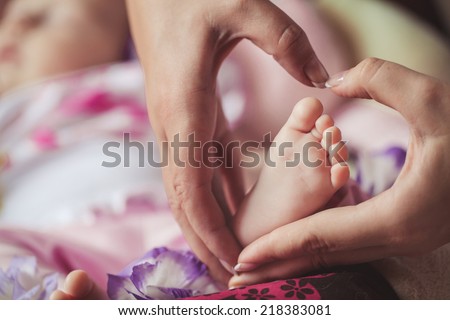Baby feet in mother hands. Tiny Newborn Baby\'s feet on female Heart Shaped hands closeup. Mom and her Child. Happy Family concept. Beautiful conceptual image of Maternity