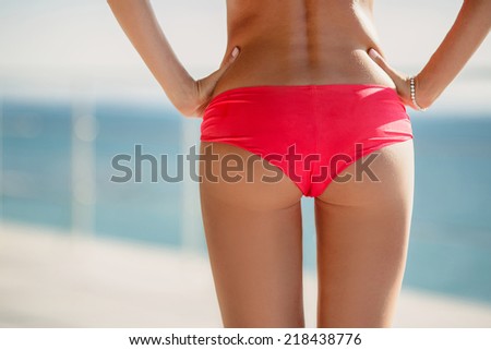 Sexy bikini woman buttocks on the beach background. Woman with beautiful body at tropical beach. Closeup of a female backside in a yellow swimsuit. A day at a beach concept.