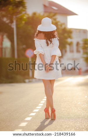 Sexy lonely woman sitting on a desert road with hat and looking at sun in summer day outdoors. Woman on the road only, on high hills and hat
