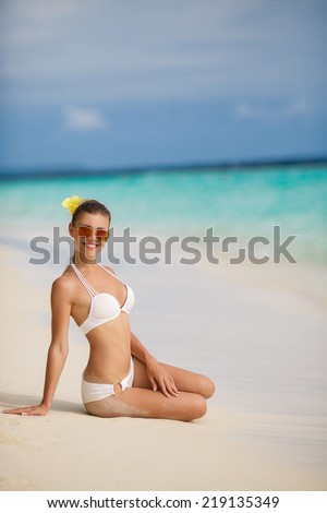 Young beautiful wet woman sitting on the sand near ocean, Bali, Indonesia, Maldives, tropical islands. Young woman sitting on sand in bikini and looking to the camera