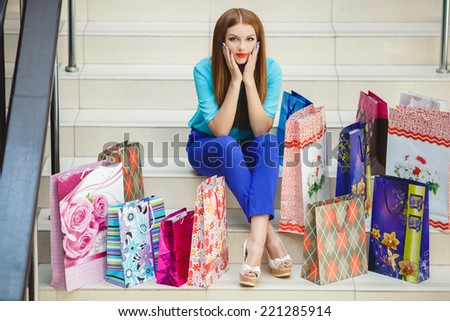 Beautiful blonde young woman wearing fashionable clothes sitting on stairs. Beautiful woman is surprised looking at her laptop, while sitting on the stairs with shopping bag