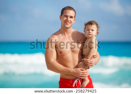 Father and little son having fun on tropical white sand beach near carebbean ocean. Man with little baby boy having fun and playing near the sea water. Ocean.
