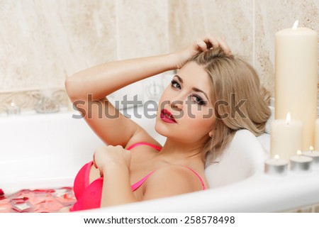 Attractive naked girl enjoys a bath with milk and rose petals. Spa treatments for skin rejuvenation. fashion interior photo of sexy beautiful woman with blond hair lying  in petals in bathtub