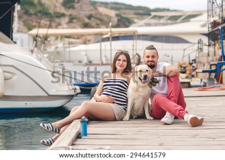 Young pregnant Family with dog Outdoors by the sea. with yachts on the background. Happy family resting outdoors in summer. Family with dog