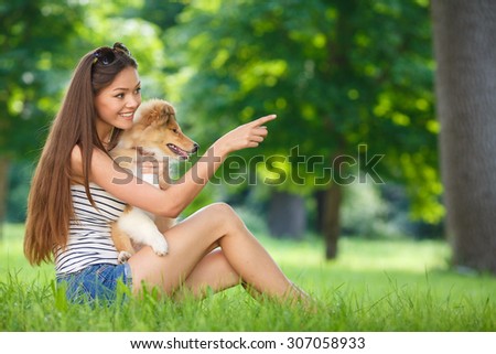 woman beautiful young happy with long dark hair in striped sweater holding dog. Young woman playing with Collie puppy outdoors in the park.
