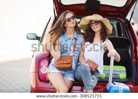 friends taking a selfie in the back of the car before leaving for vacations. Two women taking self portraits sitting in back car with suitcases. Vacation, trip concept. Road travel.