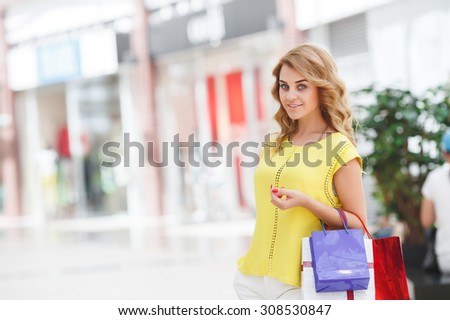 Happy beautiful woman with shopping bags stands at shop. happiness, consumerism, sale and people concept - smiling young woman with shopping bags over mall background