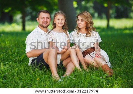 Family sitting On Grass In Park Together. Happy mother, father and daughter in the park. Portrait of happy parents and kids lying at the park