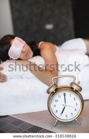 young beautiful woman sleeping on bed with alarm clock in bedroom. Sleeping woman resting in bed with alarm clock ready to wake her in the morning