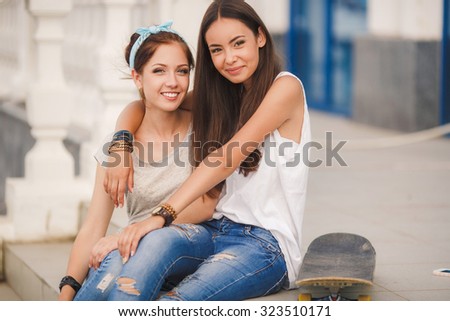 Two teen girl friends having fun together with skate board. Outdoors, urban lifestyle. Photo toned style Instagram filters.