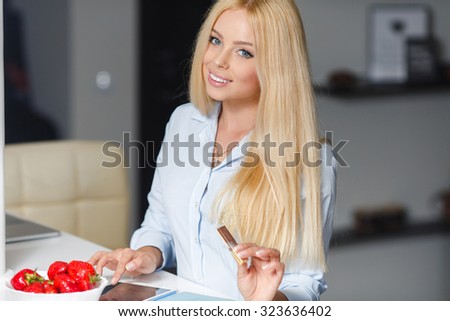 Beautiful young woman with plate of strawberries in kitchen. Smiling woman eating strawberry. Close up female face portrait. Healthy mel on a plate.