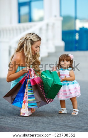 Young mother and her daughter doing shopping together. Woman with child on shopping in shopping mall with bags. Mother with baby girl with shopping bags with mall on background. Fashion and beauty.