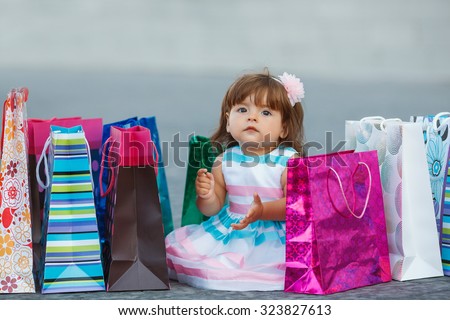 Child with shopping bags. Young girl with full of bags. Cute baby goes shopping with bags, shops in background. A little girl with the packages in the shop.Beautiful shopping girl in store