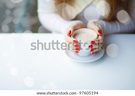 Woman\'s hands hugging a cup of coffee in a restaurant