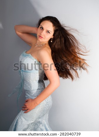 Charming romantic girl in a blue dress with long thick chocolate dense hair steaming back (waved) in a wind as a symbol of muse, youth and retro wedding