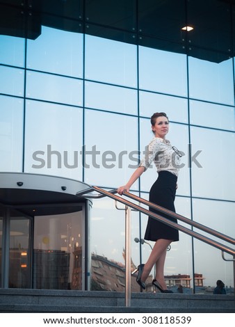 Attractive brunet businesswoman in white blouse and black skirt near business center