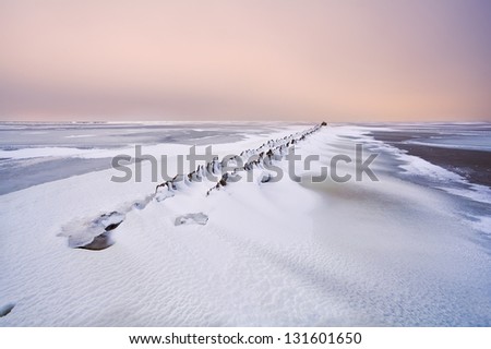 old dike in frozen north sea under snow at sunset