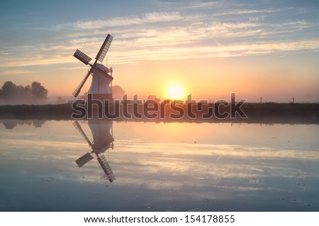 Dutch windmill reflected in river at sunrise, Groningen, Netherlands