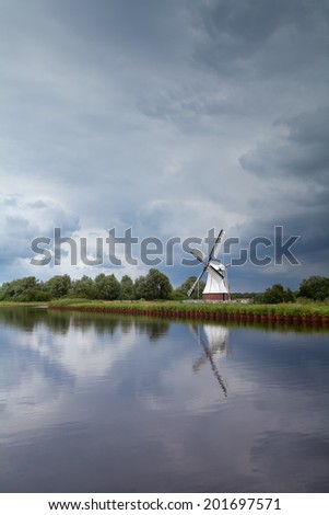 windmill by river over clouded stormy sky, Netherlands