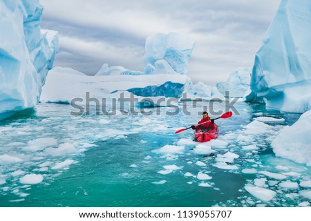 extreme tourism, winter kayaking in Antarctica, adventurous man paddling on sea kayak between icebergs