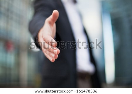 Businessman offering for handshake on office buildings background