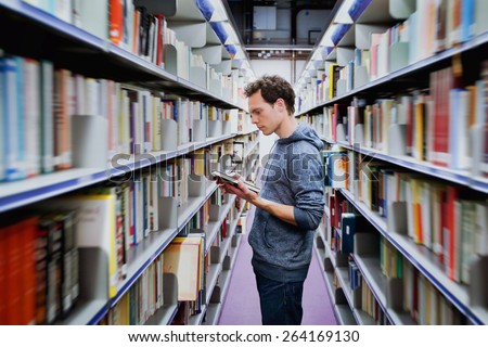 young student reading book between the shelves in the library