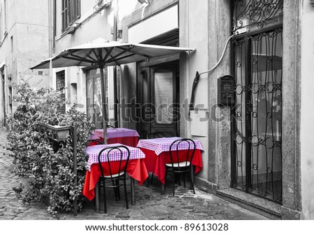 Tables and chairs for a restaurant in one of the streets of Trastevere.  In black and white and selective de-saturation