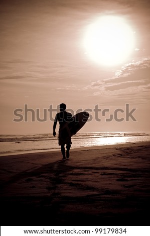 Sunset on the beach with surfer watching waves.